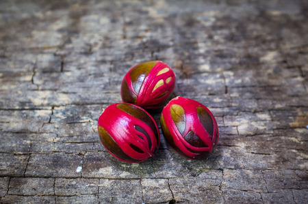 Three whole nutmeg red placenta-like cover of seed, medicinal properties. Tropical colorful plant on wooden background.の写真素材