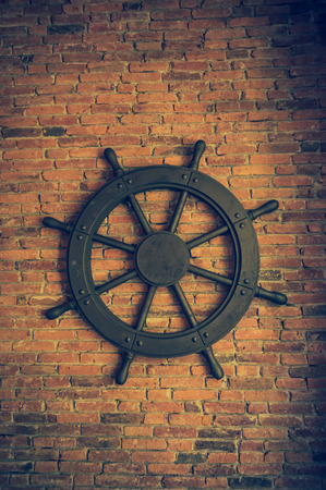 Beautiful black steering wheel for ship mounted on red brick wall background. Low key picture style.の写真素材