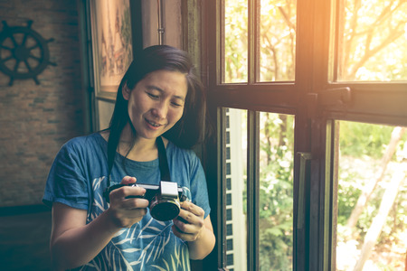 Asian woman checking and reviewing photos in digital camera near window in a external background...