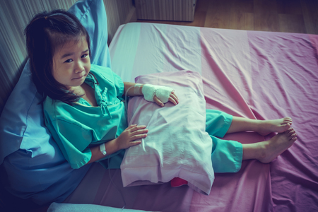 Illness asian child looking at camera. Young pretty girl admitted in hospital while saline intravenous (IV) on hand. Health care stories. Vintage film filter effect. Low key style.の写真素材
