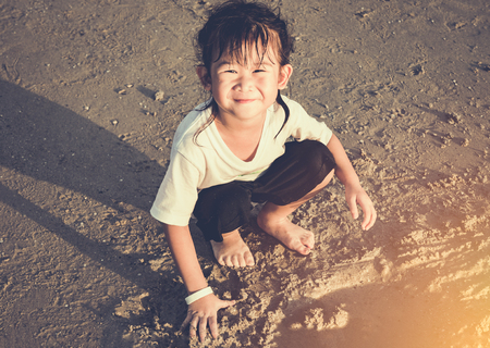 Happy asian child has fun digging in the sand. Charming young girl smiling and looking at camera on the beach. Outdoor with bright sunlight on summer day. Concept of young connecting children with nature.の写真素材