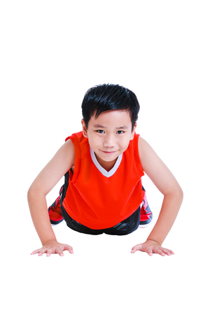 Push-ups or press-ups exercise by young asian basketball player in red uniform. Handsome child athlete smiling and looking at camera. Studio shot. Isolated on white background. Sports lifestyle.の写真素材