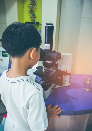 Back view of asian child observed through a microscope biological preparations in a science laboratory. Boy having education activity. Seek knowledge concept. Vintage film filter effect.の写真素材