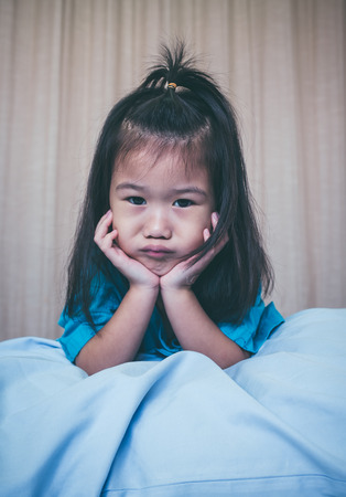 Illness asian child on sickbed and looking at camera, admitted in hospital. Unhappy girl feeling sad, bored, kid emotion. Concept for depression stress or frustration. Vintage film filter effect.の写真素材