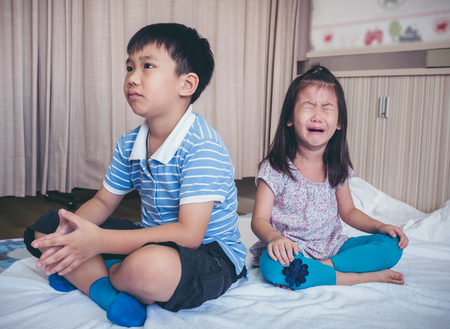Quarreling conflict of children. Asian girl has problem between brother and scream crying with tears, sadden boy sitting near by. Relationship difficulties in family concept.の写真素材