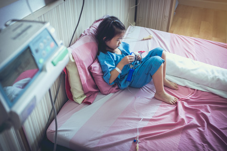 Illness asian girl admitted in hospital with infusion pump feeding IV drip. Shallow depth of field (DOF) child in focus, IV machine out of focus. Health care stories. Vintage film filter effect.の写真素材