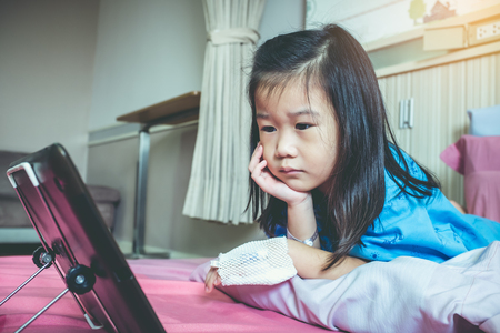 Illness asian child with saline intravenous (IV) on her hand while admitted in hospital . Cute girl looking at digital tablet. Health care stories. Vintage film filter effect.の写真素材