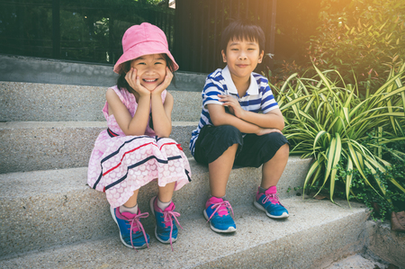 Lovely asian children ralaxing and sitting on the stair steps. Brother and sister smiling and looking at camera with bright sunlight. Happy family spending time together, loving and bonding of siblingの写真素材