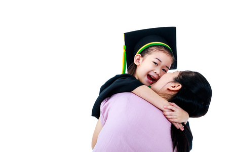 Kindergarten graduation. Happy asian child in graduation gown laughing. Mother sitting and hugging her daughter smiling happily with copy space. Isolated on white background.の写真素材