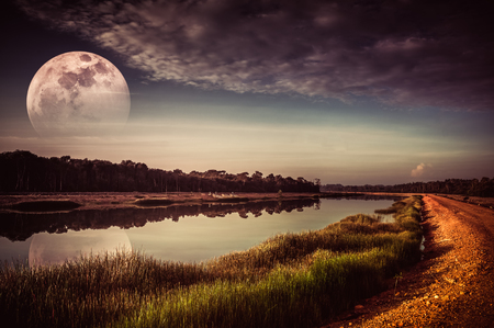 Beautiful landscape of sky with cloud and fade half super moon above silhouettes of trees at riverside. Serenity nature background. Early evening outdoor. The moon taken with my camera.の写真素材