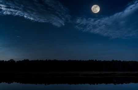 Beautiful landscape of blue sky with cloud and bright full moon above silhouettes of trees at seaboard. Serenity nature background, outdoor at nighttime. The moon taken with my camera.の写真素材