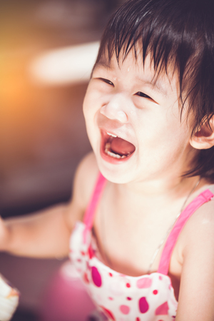 Closeup charming asian child smiling happily. Cute Chinese girl having fun and laughing with drop on her face.  Daytime with bright sunlight. Vintage film filter effect.の写真素材