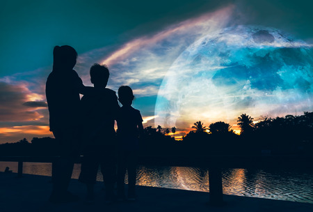 Silhouette of mother with her son and daughter looking at supermoon on colorful sky . Beautiful nature background. Spending time outdoors, cozy mood. The moon taken with my camera.の写真素材
