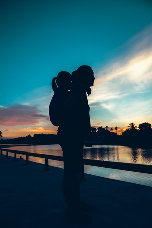 Silhouette of mother giving piggyback ride to her daughter in the morning, cozy mood. Colorful pastel sky sunrise, serenity background. Happy family spending time together. Travel on vacation.の写真素材