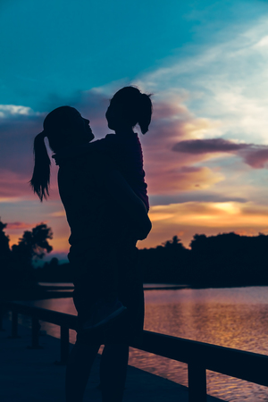 Silhouette of mother carrying her daughter and enjoying view in the morning, cozy mood. Colorful pastel sky sunrise, serenity background. Happy family spending time together. Travel on vacation.の写真素材
