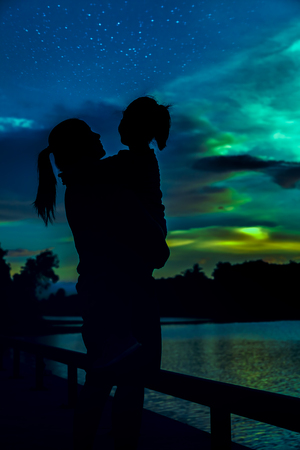 Silhouette of mother and her daughter enjoying view with many stars on colorful sky. Serenity nature background. Happy family spending time together. The moon taken with my camera.の写真素材