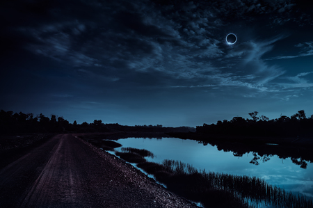 Amazing scientific natural phenomenon. The Moon covering the Sun. Total solar eclipse with diamond ring effect glowing on blue sky above silhouettes of trees. Serenity nature background.の写真素材