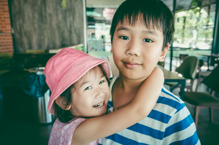 Adorable asian girl smiling with perfect smile and put her's arm around brother's shoulder in coffee...