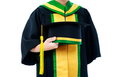 Kindergarten graduation. Child in graduation gown holding cap, studio shot. Education concept. Isolated on white backgroundの写真素材