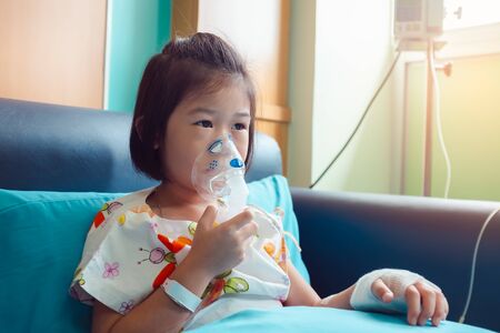 Sad asian child holds a mask vapor inhaler for treatment of asthma. Breathing through a steam...