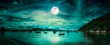 Beautiful panorama nature landscape. Beach by the sea with mountains and full moon at nighttime.Many fishing boats Floating in the bay of the sea in southern Thailand. The moon taken with my camera.の写真素材