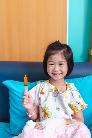 Close up of illness asian child admitted in hospital with saline intravenous (IV) on hand. Girl feeling happy while taking medicine syrup, facial expression. Health care stories.の写真素材