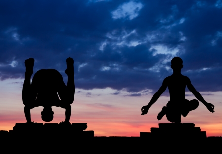 Silhouette of a man in yoga position, upside down, and standing with one foot on a brick wall amid cloudy の写真素材