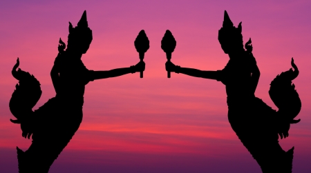 Silhouette of two black half-bird half-woman, who is holding a torch on the morning skyの写真素材