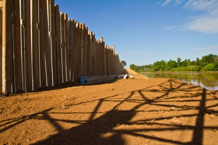 Pillars and concrete dam to prevent water erosion and the shadow of a large crane on the river の写真素材