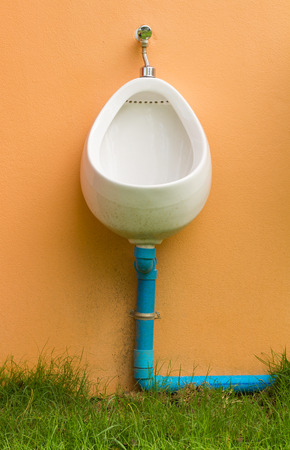 Urinal installed on a concrete wall with brown grass beneath.の写真素材