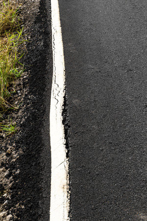 Close-up side of the new road surface cracks in a long white line.の写真素材
