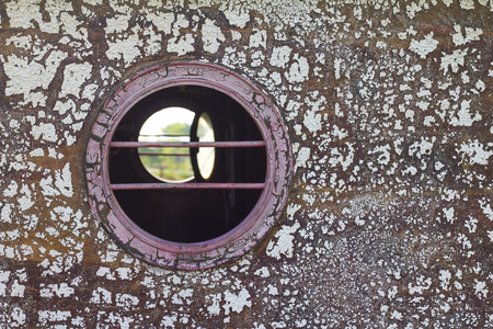 Close round peephole of old vintage wooden boat, which weathered and peeling paint.