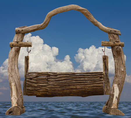 Old wooden chair swing seat hanging in the middle of the river, cloudy sky in the background.の写真素材