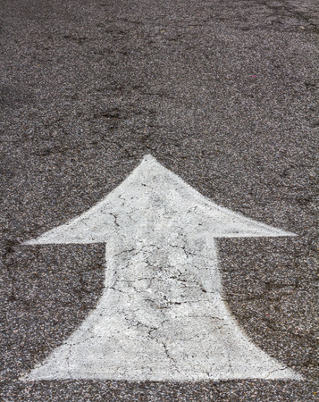 Background white arrows painted on the floor next to a paved road show to symbolize quaint.