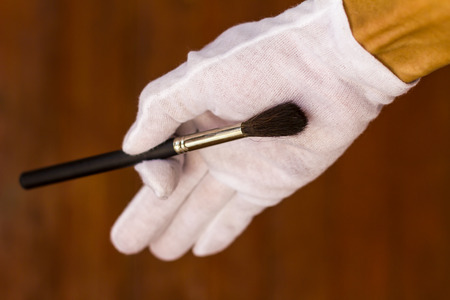 Close up of men wearing white gloves hold paint brush with a wooden wall blurred background.