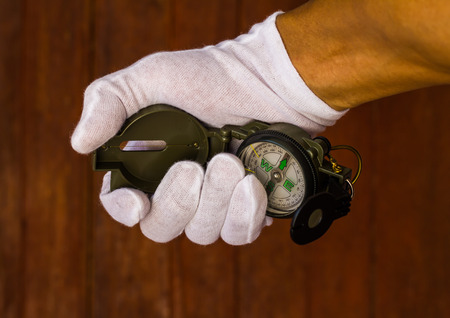 White gloved hand holding a compass for direction, with the old wooden wall as a backdrop.の写真素材