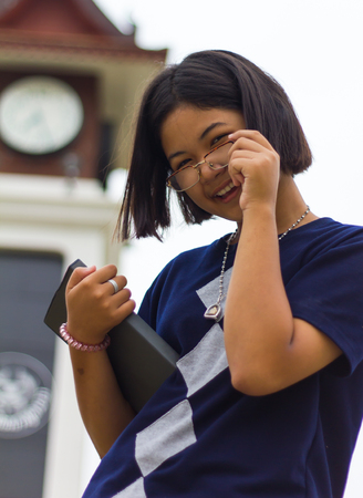 Low angle close-teen girl, wearing glasses reading a beaming near the clock tower.の写真素材