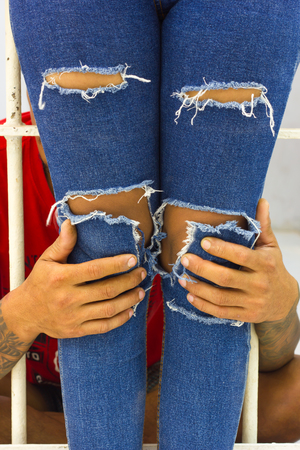 Man hands are holding the leg of his girlfriend, who wears torn jeans standing outside the prison.の写真素材