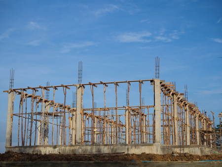 Concrete structural columns and beams of a house located on the mound with the sky as a backdrop.