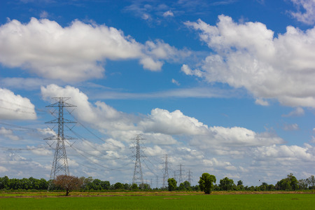 High voltage poles towering scenery of rice fields, green countryside, with cloudy sky as a...
