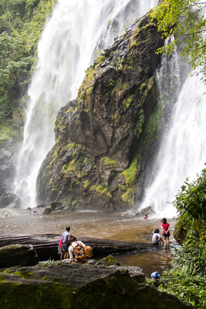 Large waterfall on the rocks with people standing and walking in the water below.のeditorial素材
