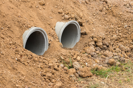 Concrete pipes are buried in dirt gravels that are dug up for drainage under rural roads.