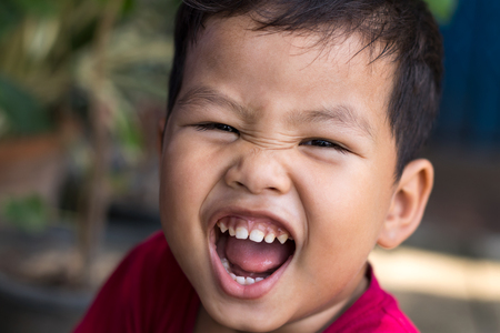Close-up image of Thai boy face is open mouth and looks like a giant yelling and laughing fun.の写真素材