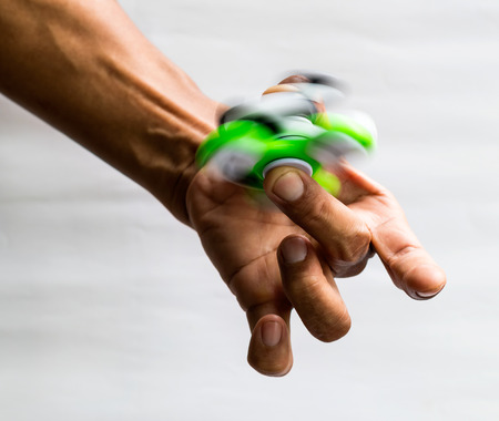 Close-up image of green, white and black hand spinner, a popular toy in male fingers.