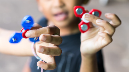 Close-up image of hand spinner, which is a popular toy in the hands of a boy with a girl blurred as a backdrop.の写真素材
