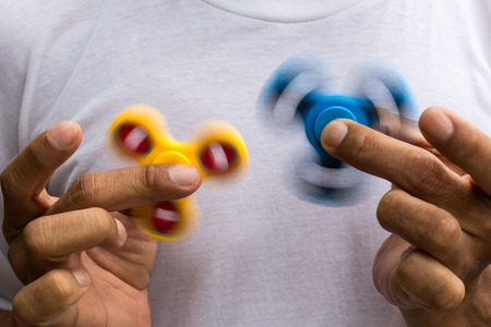 Both blue and yellow spinner hands are in the fingers of a man who wears a white t-shirt.の写真素材