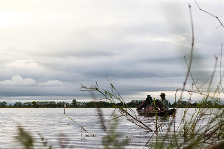 Low angle looking through the grass weeds to Thailand which two grandparents who are boating, fishing villages on the lake.の写真素材