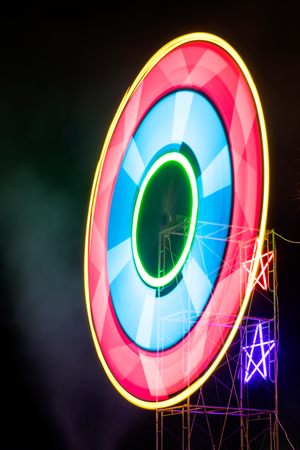 Neon light rotates in a colorful circle on the scaffolding at the Thai temple festival at night.の写真素材