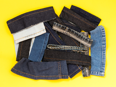 Various pieces of jeans left over from the sewing thread are placed on a yellow background.
