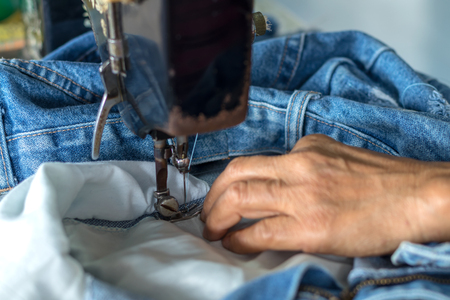 Close-up of an elderly woman working on repairing jeans with an old sewing machine with skill and expertise.の写真素材